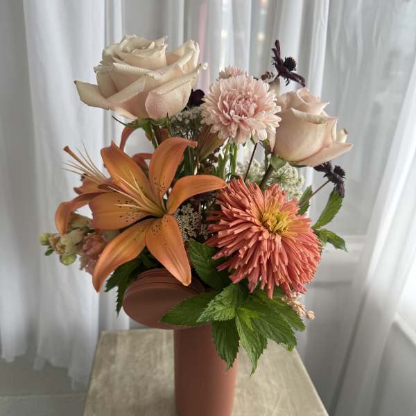 Peach and cream floral arrangement in a tall vase with roses and lilies