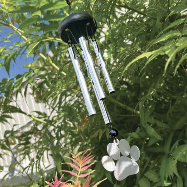 Metal wind chime hanging among green foliage with a paw-shaped ornament