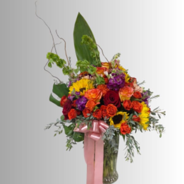 Tall mixed bouquet of roses and sunflowers in a glass vase with a pink ribbon