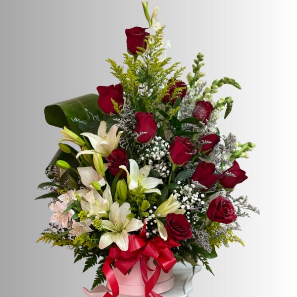 Red roses and white lilies arranged in a pink box with a red ribbon.
