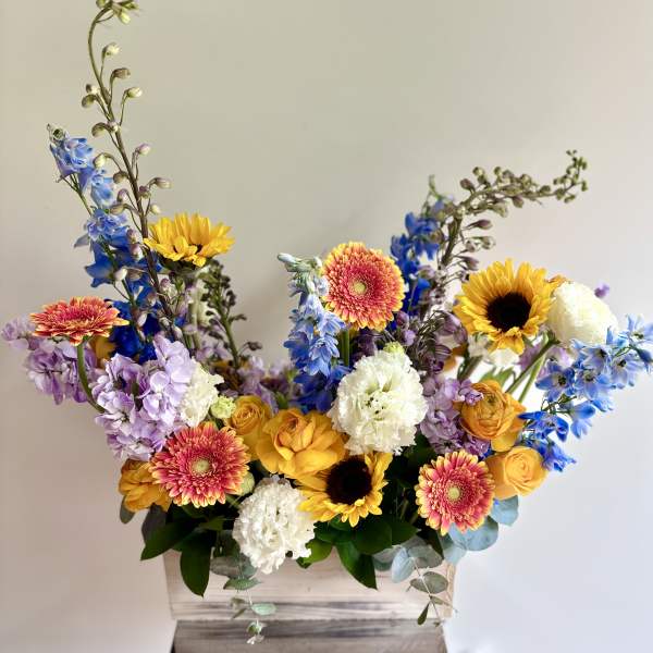 Mixed bouquet in a wooden box with sunflowers, gerbera daisies, and blue flowers