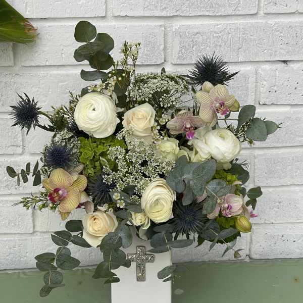 White floral arrangement in a square vase with a cross ornament