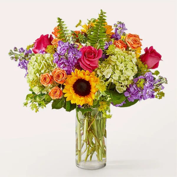 Colorful bouquet of roses, sunflowers, and purple blooms in a glass vase
