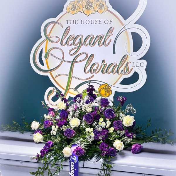 Purple and white rose arrangement on a silver casket with a ribbon