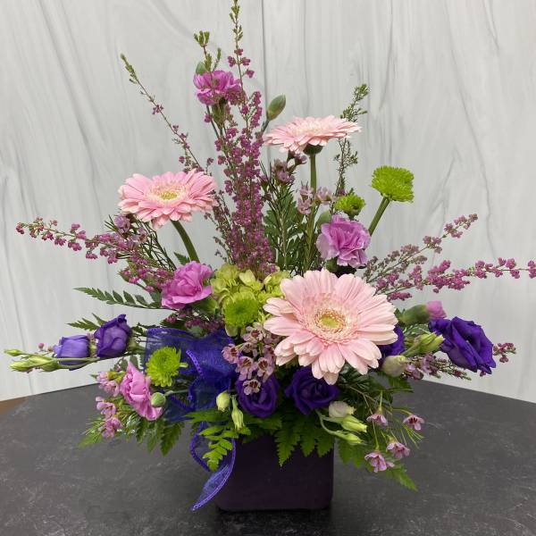 Pink and purple mixed flower arrangement in a dark square vase