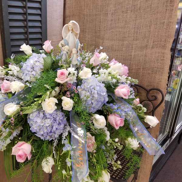 Large pastel floral spray with roses and hydrangeas around a religious figurine