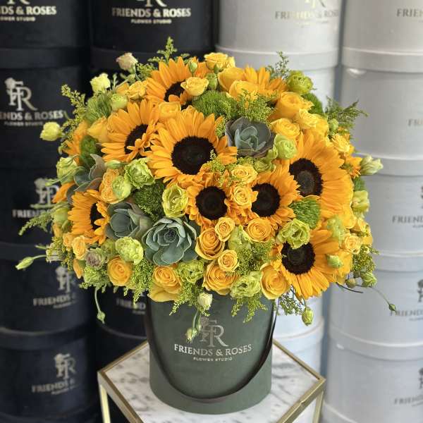 Bouquet of sunflowers and yellow roses in a green hatbox.