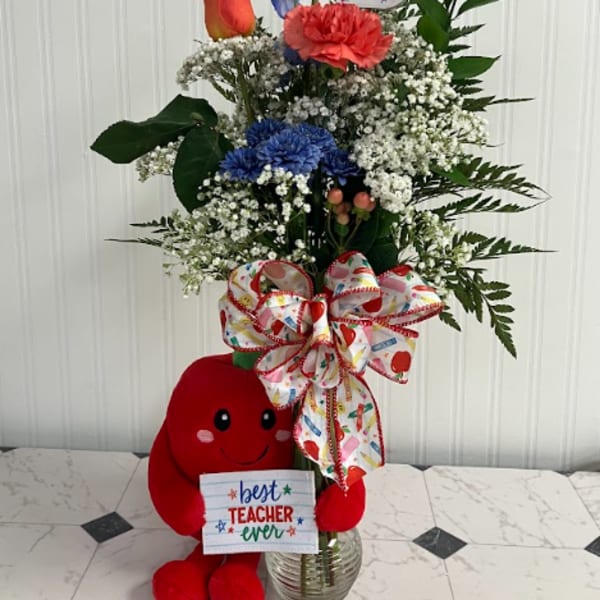 Tall mixed flower arrangement with a plush teacher bear and gift sign in a glass vase