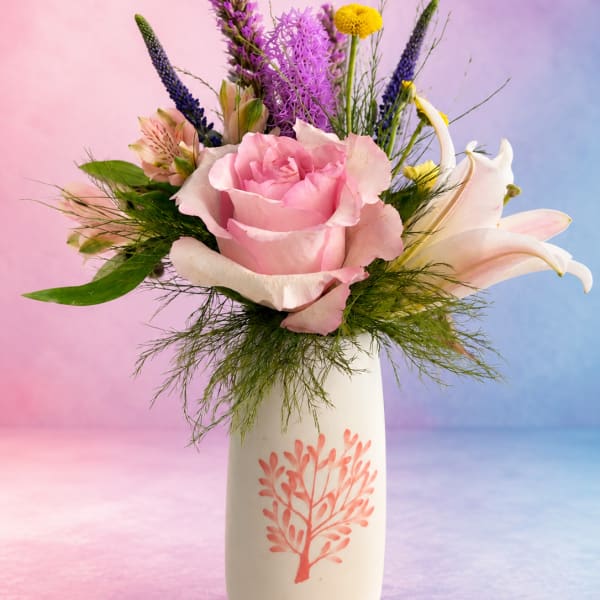 Pink rose bouquet with lilies and purple accents in a white vase