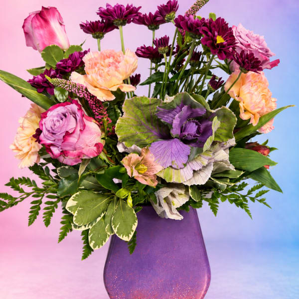 Mixed bouquet of pink, peach, and purple flowers in a purple vase