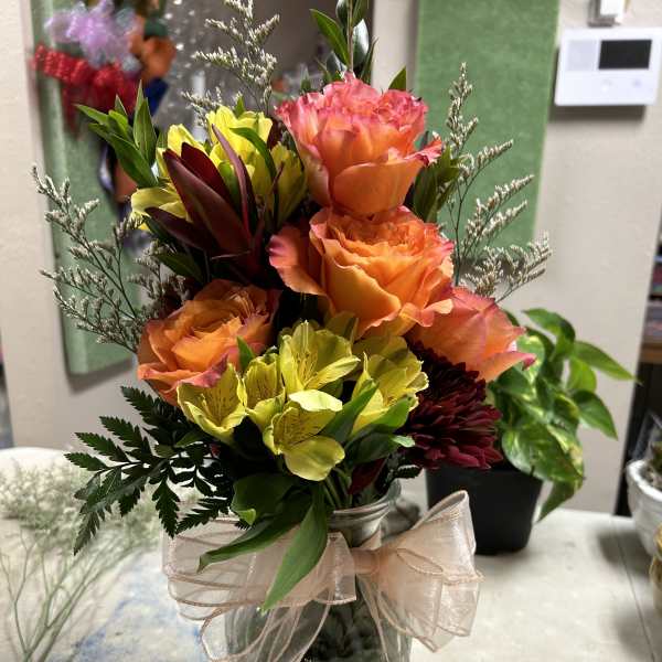 Bouquet of orange roses and yellow flowers in a glass vase with a ribbon