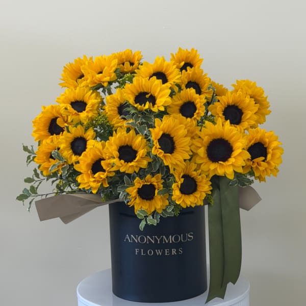 Bouquet of yellow sunflowers in a dark round box with ribbon