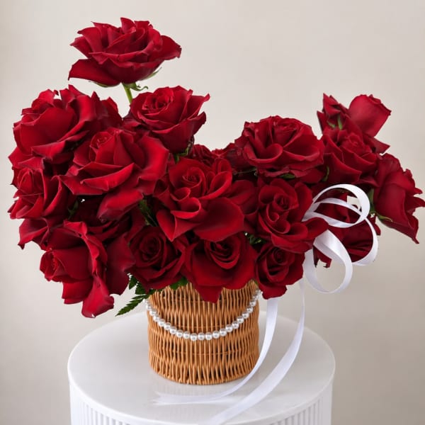 Red roses arranged in a wicker basket with a white ribbon and pearl trim