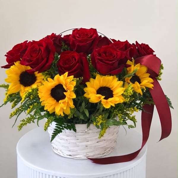 Red roses and yellow sunflowers in a white basket with a burgundy ribbon