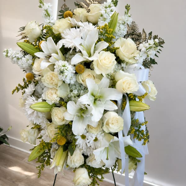 White floral standing spray with roses, lilies, and daisies on a ribboned easel