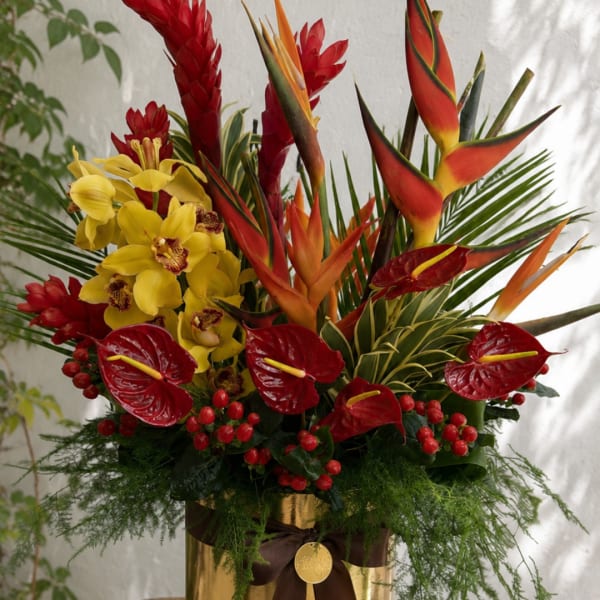 Tropical arrangement with red and yellow flowers in a gold container