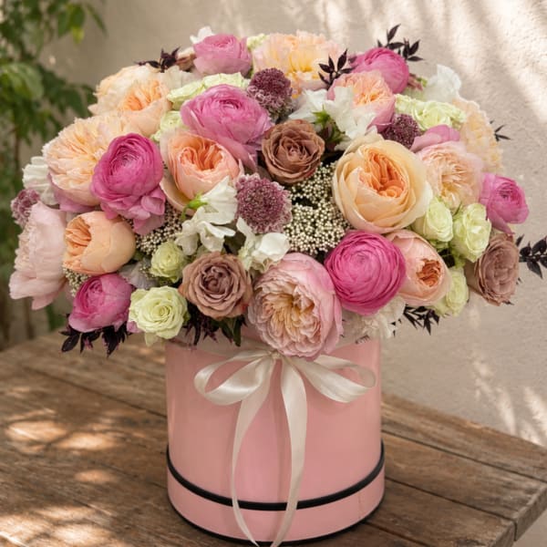 Pink and peach roses arranged in a round pink box with a ribbon
