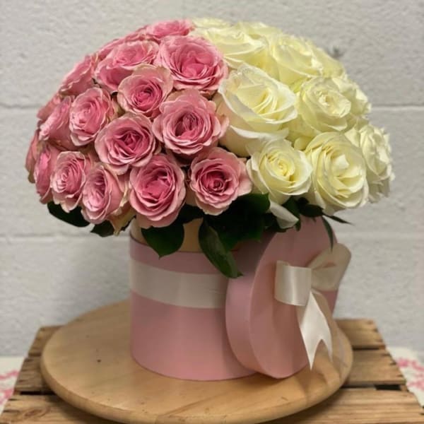 Pink and cream roses arranged in a round hatbox with a ribbon bow