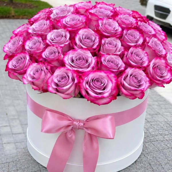 Pink roses arranged in a white round box with a pink ribbon bow