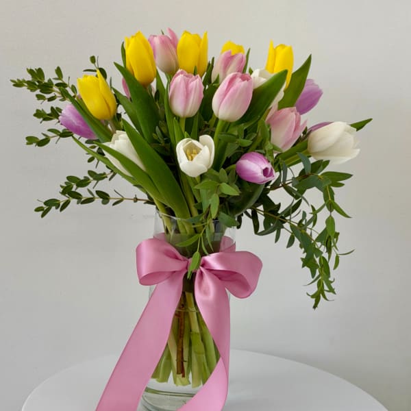 Bouquet of pink, yellow, and white tulips in a glass vase with a pink ribbon