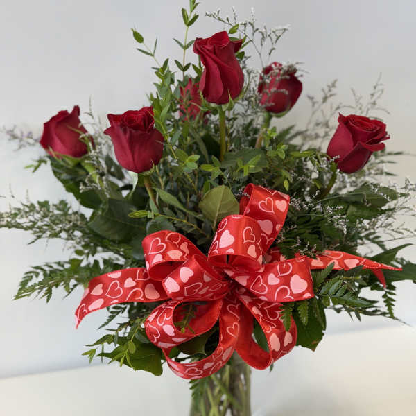Red roses in a clear glass vase with a heart-patterned ribbon