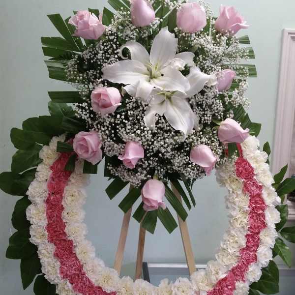 Pink roses and white lilies in a standing floral wreath with a pink-and-white garland