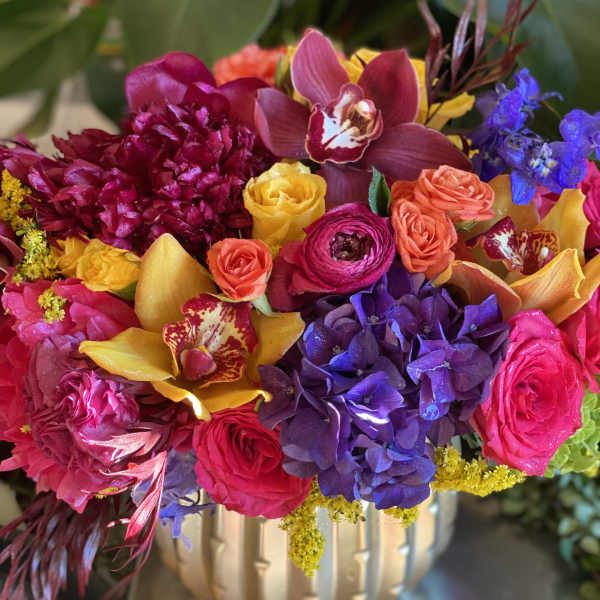 Colorful bouquet in a gold vase with orchids, roses, hydrangeas, and ranunculus