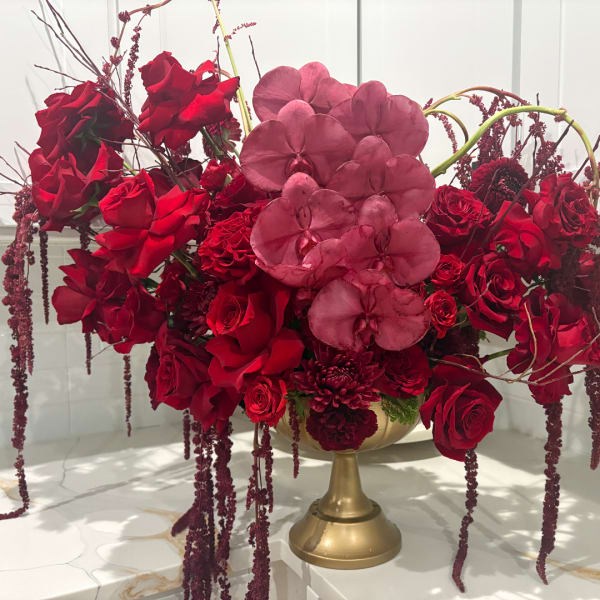 Red rose arrangement with pink orchids in a gold pedestal vase