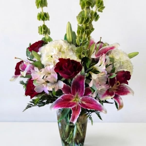 Mixed bouquet of lilies, hydrangeas, and red blooms in a glass vase