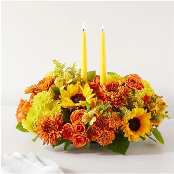 Yellow and orange floral centerpiece with two lit taper candles