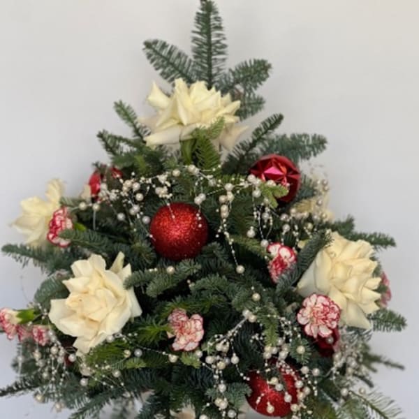 Christmas arrangement with white flowers, red ornaments, and evergreen branches in a glass vase