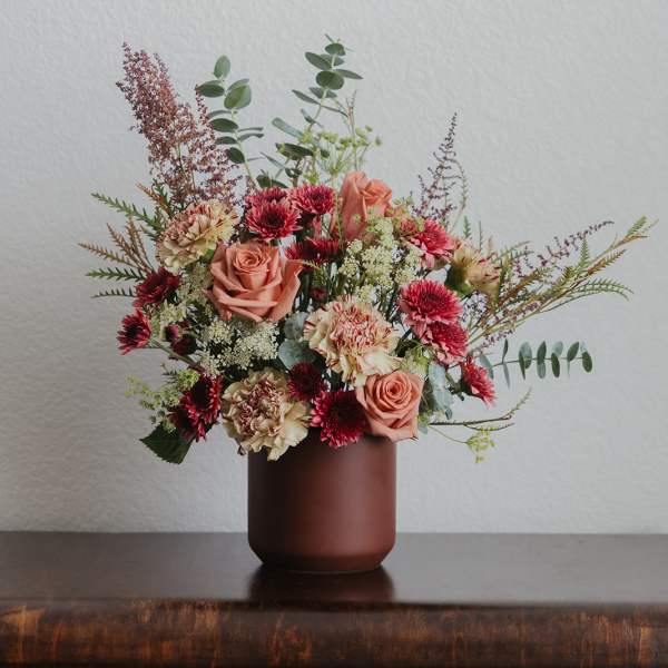 Mixed bouquet of peach roses and burgundy flowers in a brown vase