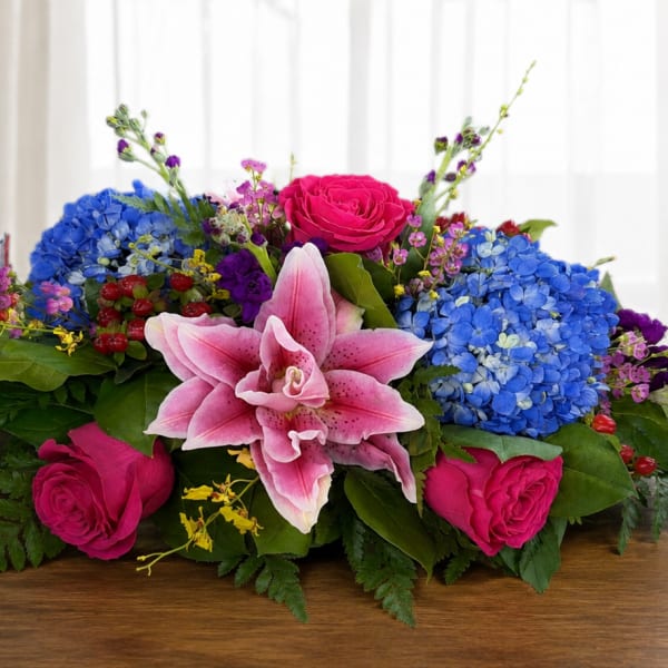 Low floral centerpiece with pink lilies, hot pink roses, and blue hydrangeas