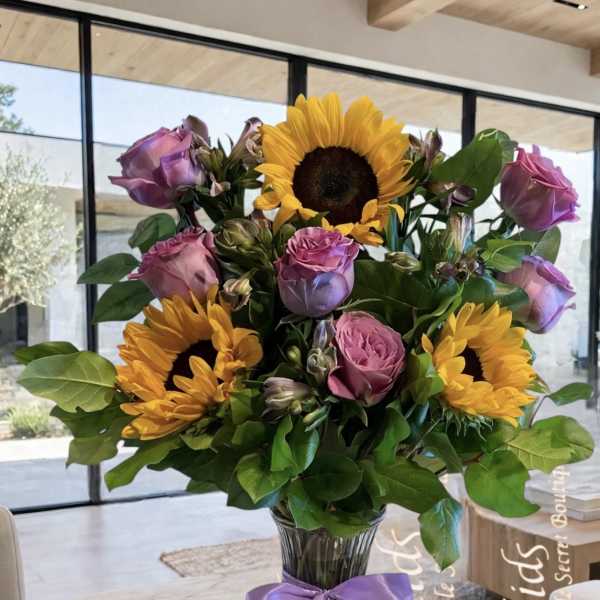 Bouquet of sunflowers and pink roses in a glass vase with a purple ribbon