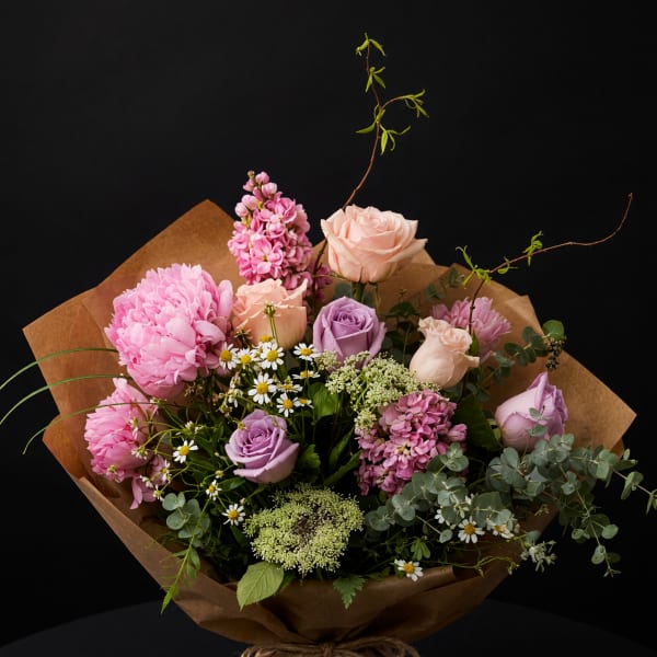 Bouquet of pink and lavender roses with mixed blooms in brown paper wrap