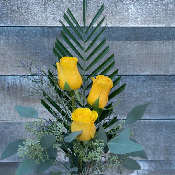 Three yellow roses in a clear glass vase with mixed greenery