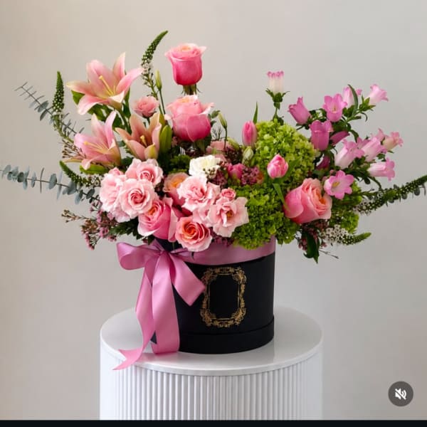 Pink mixed flower arrangement in a black hatbox with a pink ribbon