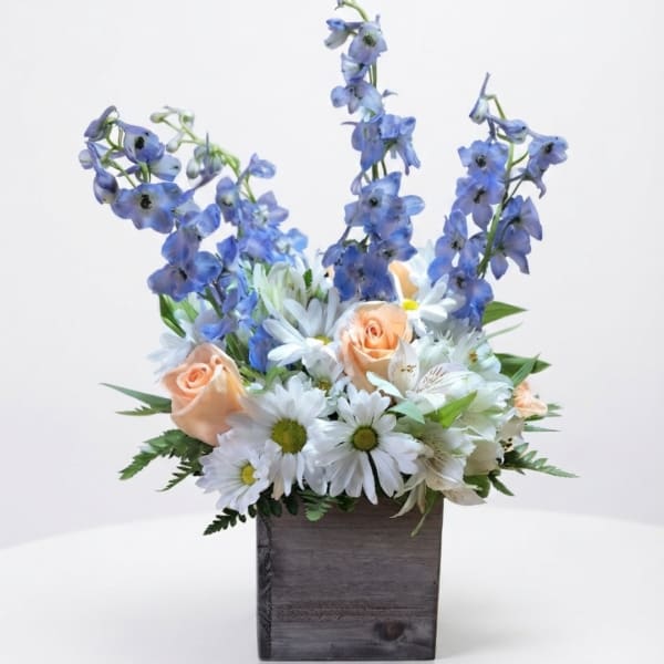 Blue delphinium and peach roses in a wooden box with white daisies