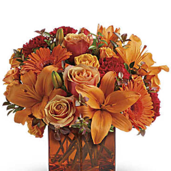 Orange and red flower arrangement in a square glass vase