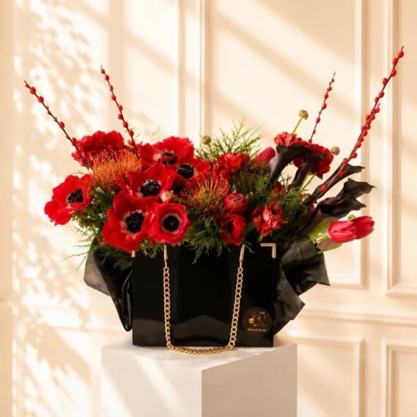 Red floral arrangement in a black gift bag with gold chain handles