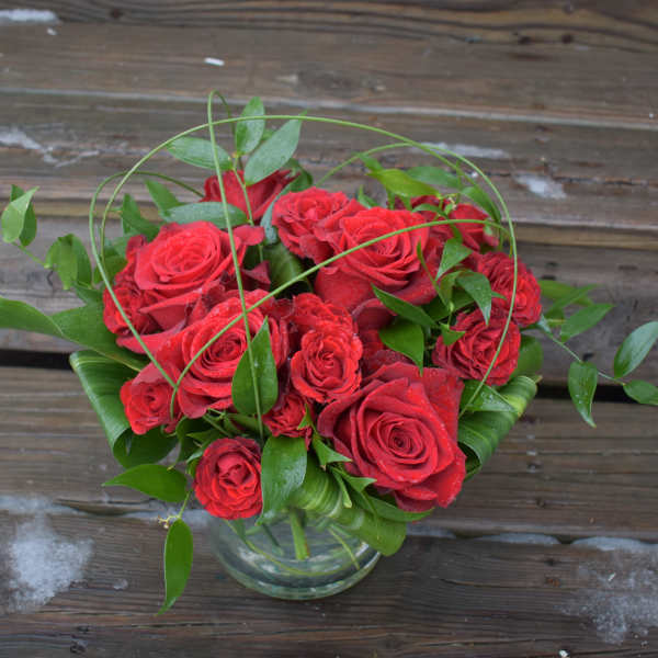 Red roses arranged in a clear glass vase with green foliage