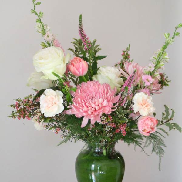 Pink and white mixed flower arrangement in a green glass vase