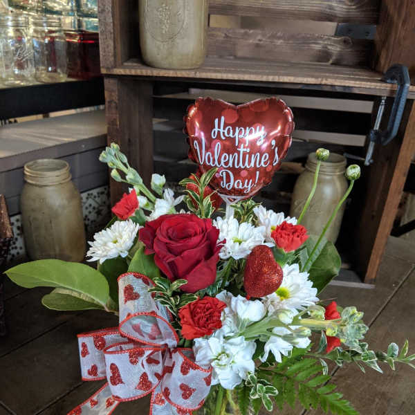 Red and white flower arrangement in a glass vase with a heart balloon