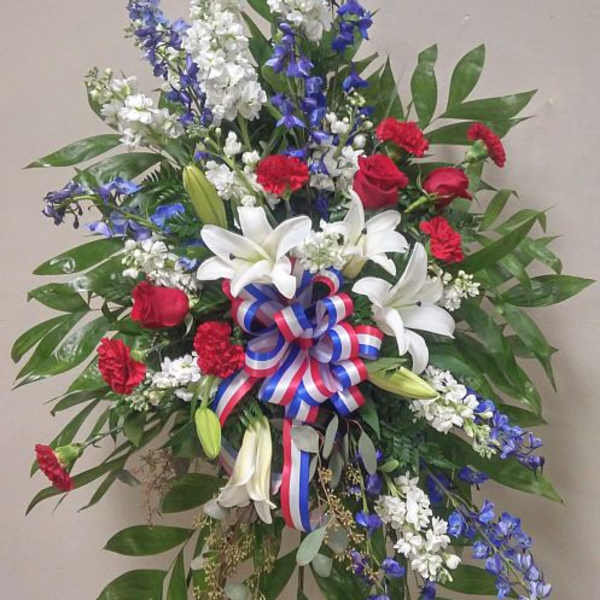 Standing floral spray with red roses, white lilies, and blue flowers