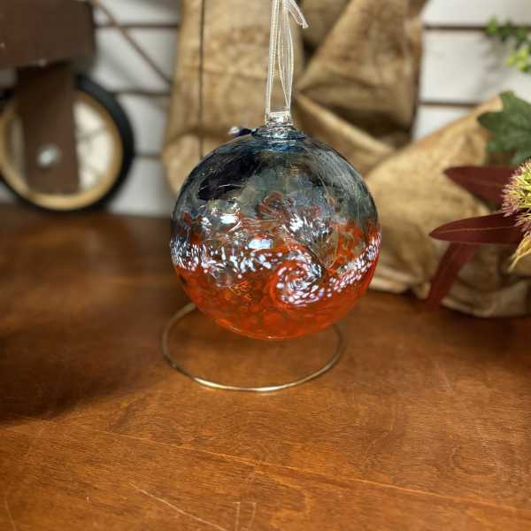 Glass ornament with blue and orange swirls hanging on a metal stand