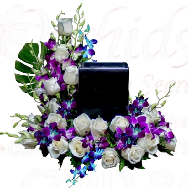 White roses and purple orchids arranged around a black rectangular vase
