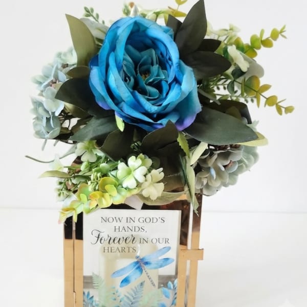 Blue rose arrangement in a gold lantern with a memorial card