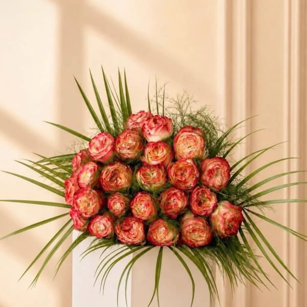 Round bouquet of pink and cream roses with long palm-like leaves