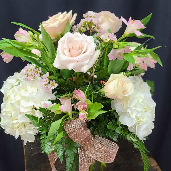 Pink and white roses arranged with hydrangeas in a glass vase