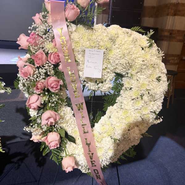 Heart-shaped floral tribute with pink roses and white flowers, tied with a pink ribbon